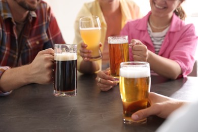 Photo of Friends with glasses of beer at grey table indoors, selective focus