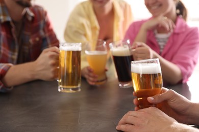 Photo of Friends with glasses of beer at grey table indoors, selective focus