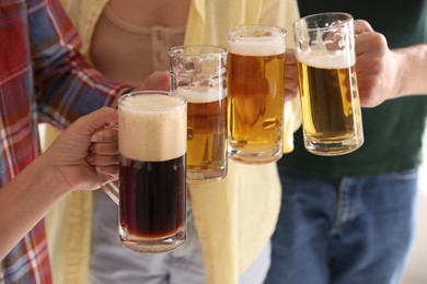 Photo of Friends clinking glass mugs of beer indoors, closeup