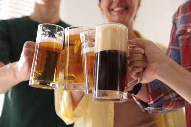Photo of Friends clinking glass mugs of beer indoors, low angle view