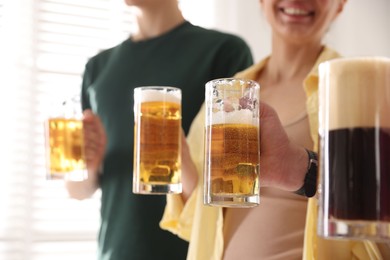 Photo of Friends with glass mugs of beer indoors, closeup