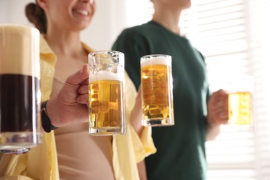 Photo of Friends with glass mugs of beer indoors, closeup