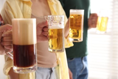 Photo of Friends with glass mugs of beer indoors, closeup