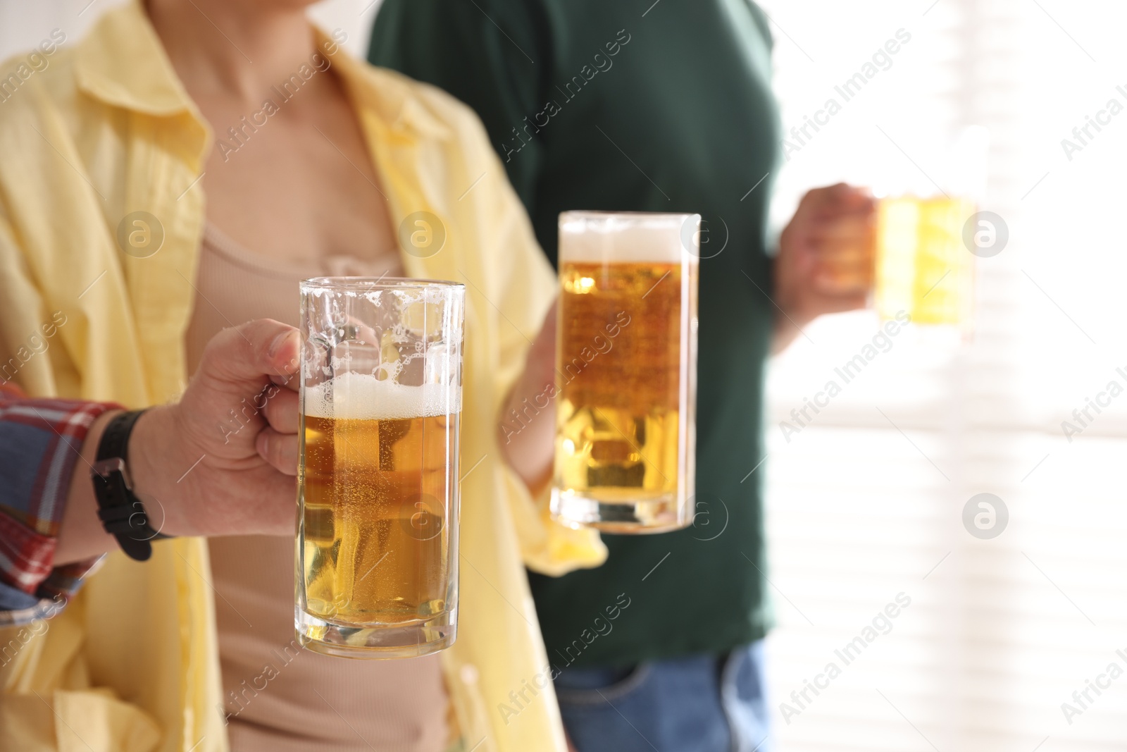 Friends with glass mugs of beer indoors, closeup. Space for text Photo of Friends with glass mugs of beer indoors, closeup. Space for text