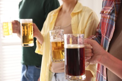 Photo of Friends with glass mugs of beer indoors, closeup