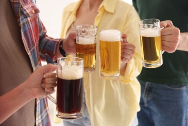 Photo of Friends clinking glass mugs of beer indoors, closeup