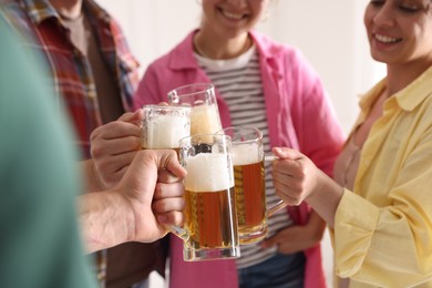 Photo of Friends clinking glass mugs of beer indoors, closeup