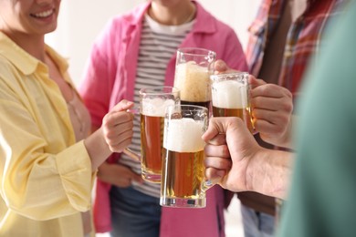 Photo of Friends clinking glass mugs of beer indoors, closeup