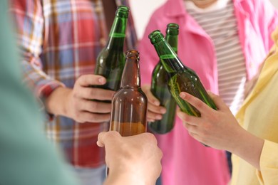 Photo of Friends clinking bottles of beer indoors, closeup