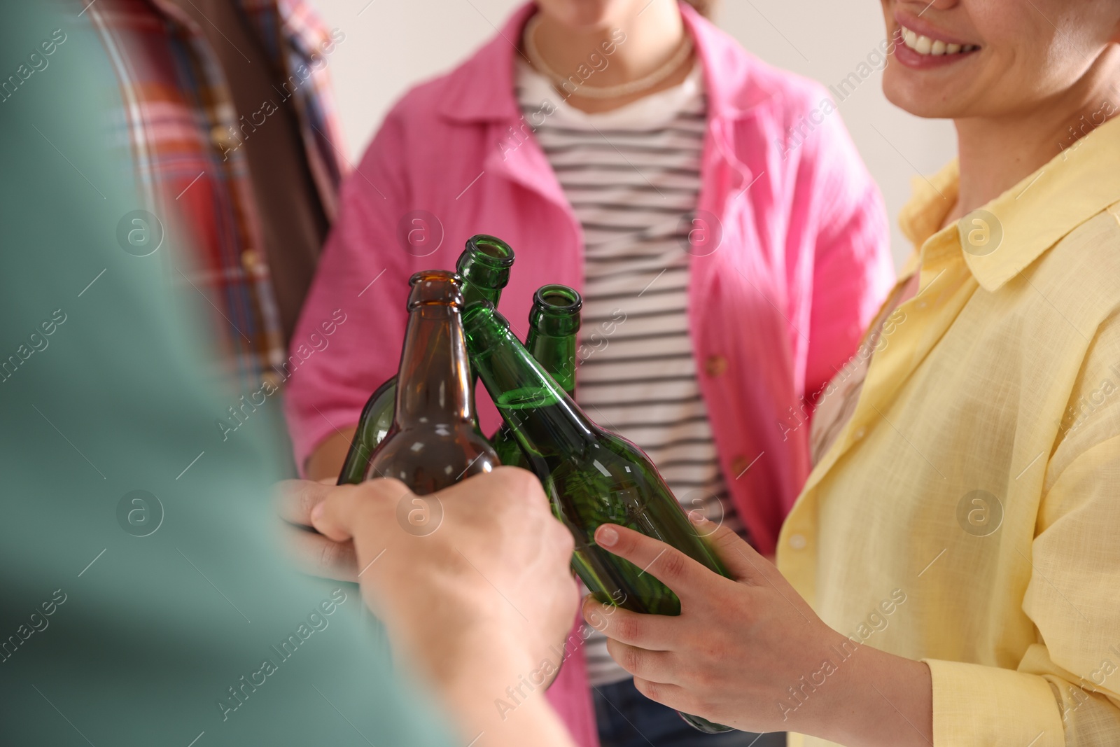 Photo of Friends clinking bottles of beer indoors, closeup