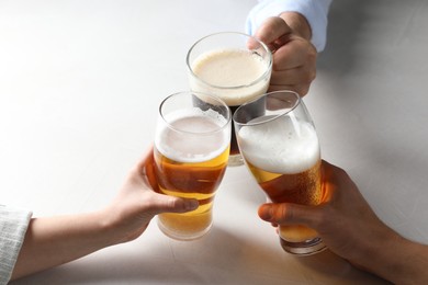 Photo of Friends clinking glasses of beer at white table, above view