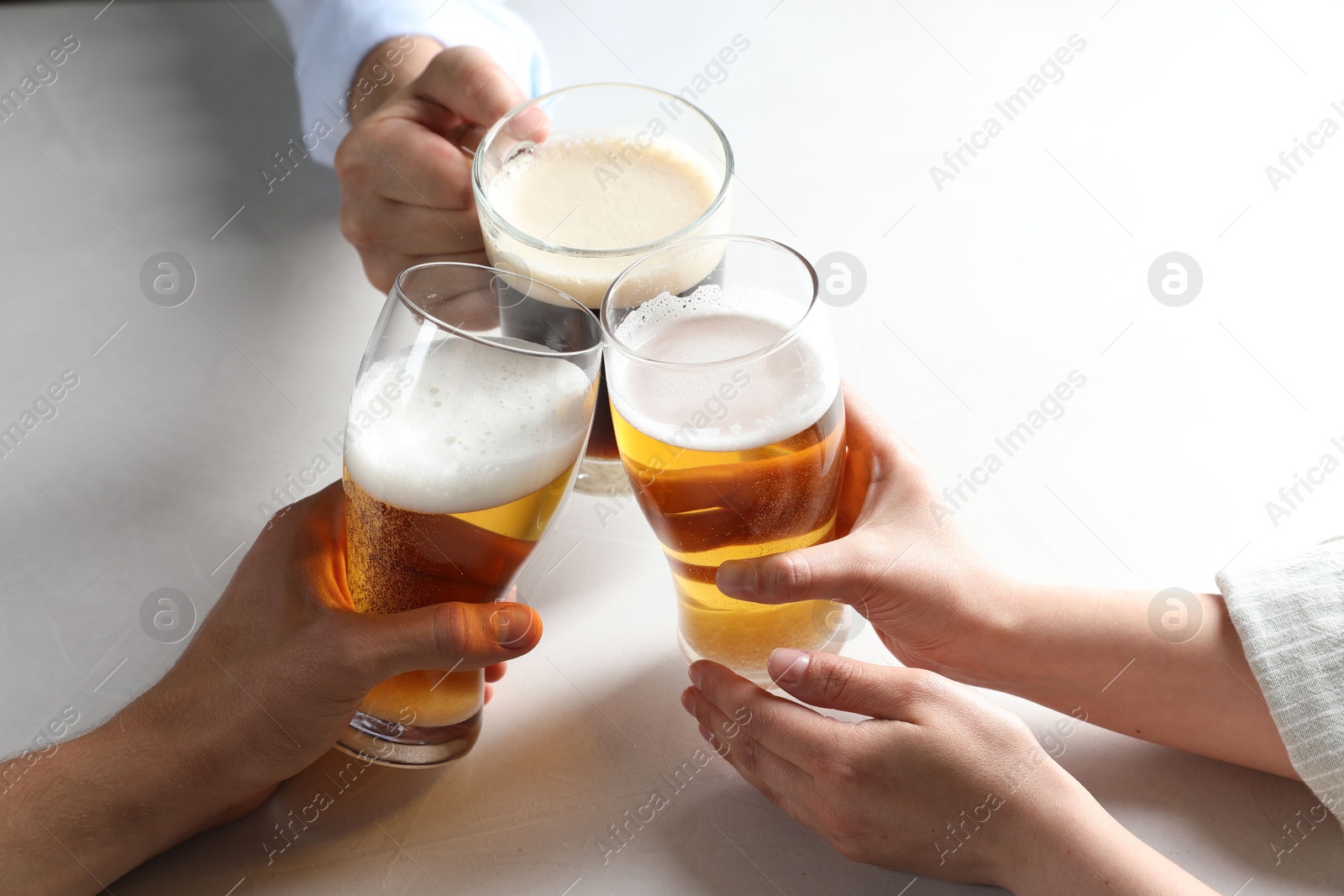 Photo of Friends clinking glasses of beer at white table, above view