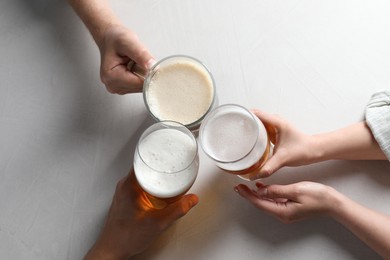 Photo of Friends clinking glasses of beer at white table, top view