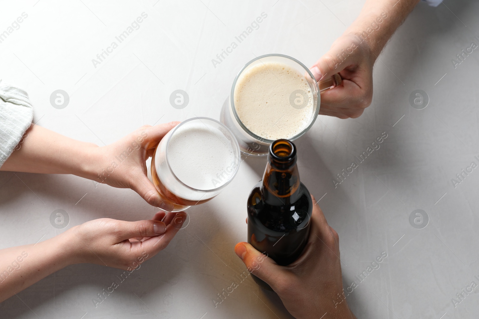 Friends clinking glasses and bottle of beer at white table, top view Photo of Friends clinking glasses and bottle of beer at white table, top view