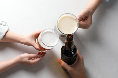 Photo of Friends clinking glasses and bottle of beer at white table, top view