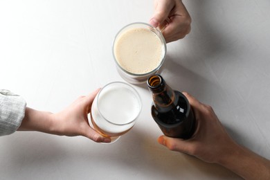 Photo of Friends clinking glasses and bottle of beer at white table, top view