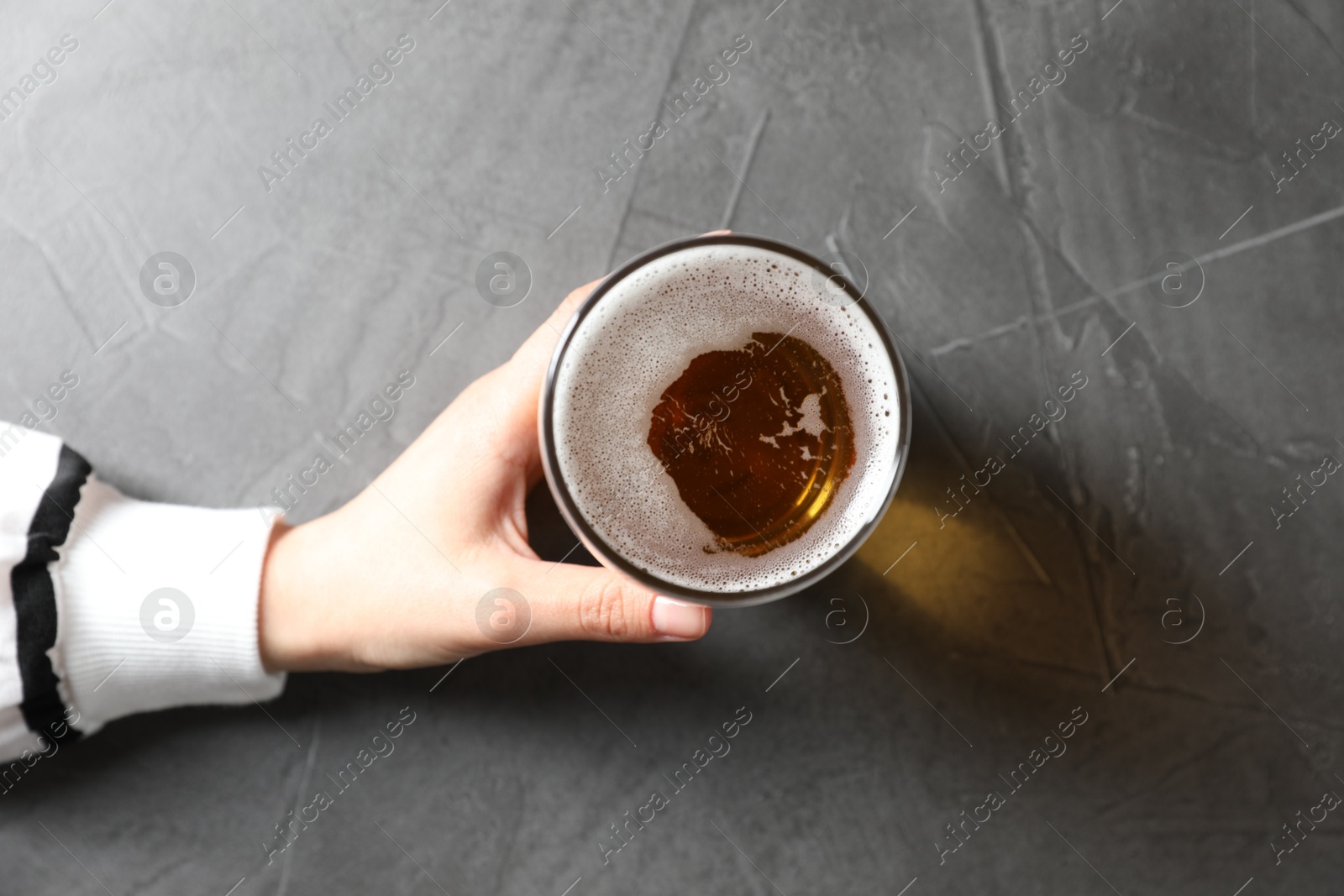Photo of Woman with glass of beer at grey table, top view