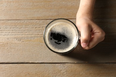 Photo of Man with glass mug of beer at wooden table, top view. Space for text