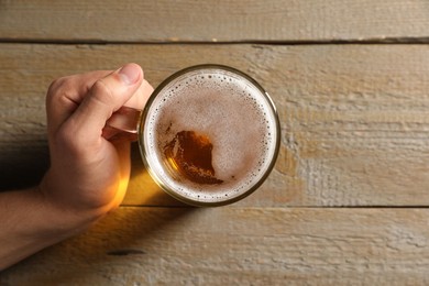 Photo of Man with glass mug of beer at wooden table, top view