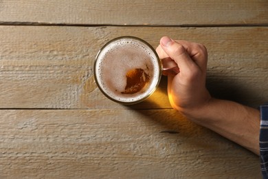 Photo of Man with glass mug of beer at wooden table, top view. Space for text