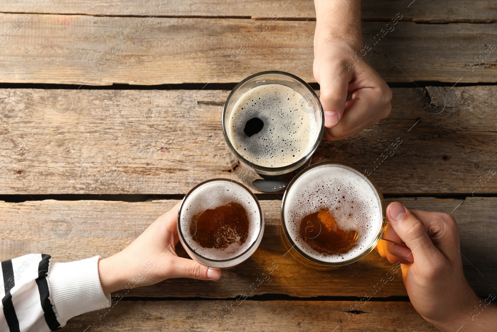 Photo of Friends with glasses of beer at wooden table, top view. Space for text