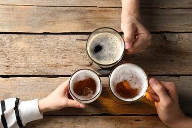 Photo of Friends with glasses of beer at wooden table, top view. Space for text