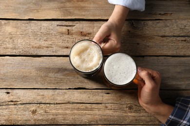Photo of Friends with glass mugs of beer at wooden table, top view. Space for text