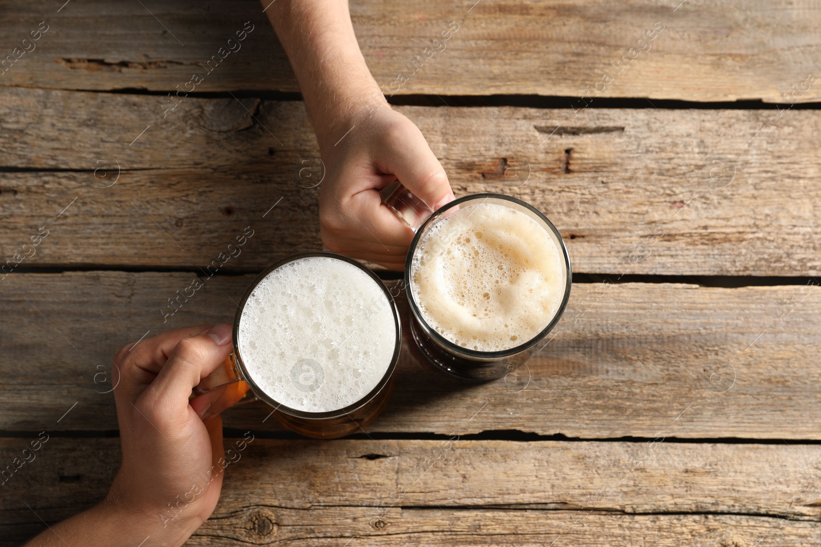 Photo of Friends with glass mugs of beer at wooden table, top view
