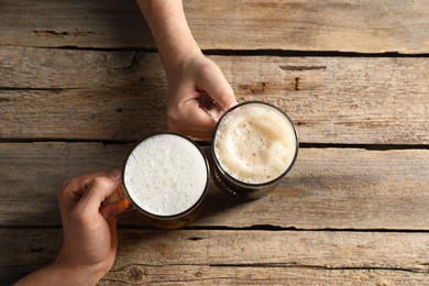 Photo of Friends with glass mugs of beer at wooden table, top view