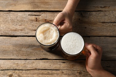 Photo of Friends with glass mugs of beer at wooden table, top view