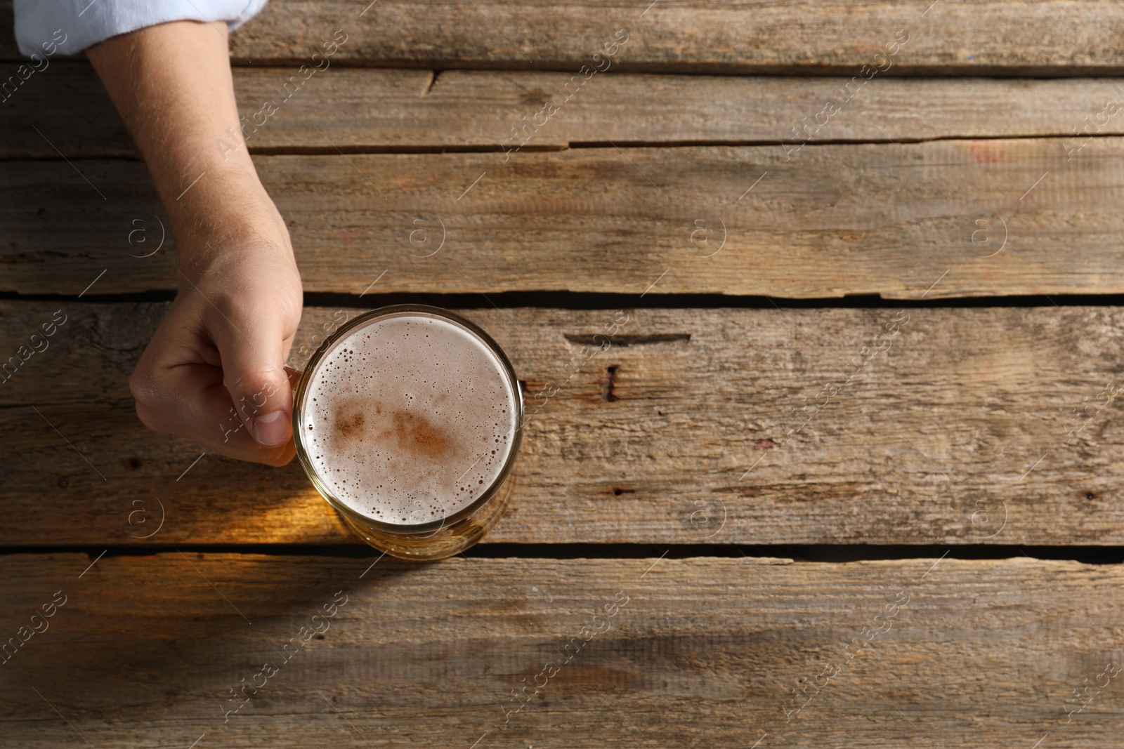 Photo of Man with glass mug of beer at wooden table, top view. Space for text