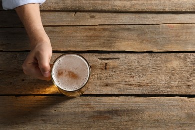 Photo of Man with glass mug of beer at wooden table, top view. Space for text