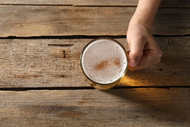 Photo of Man with glass mug of beer at wooden table, top view. Space for text