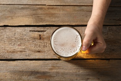Photo of Man with glass mug of beer at wooden table, top view. Space for text