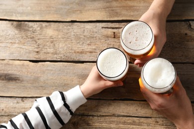 Photo of Friends with glasses of beer at wooden table, top view. Space for text