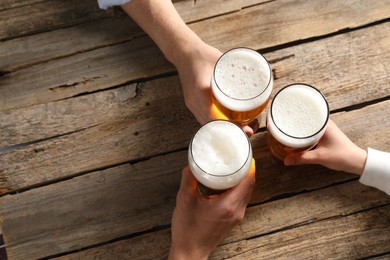 Photo of Friends with glasses of beer at wooden table, top view. Space for text
