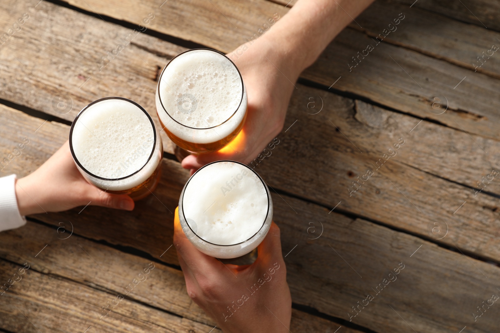 Photo of Friends with glasses of beer at wooden table, top view. Space for text