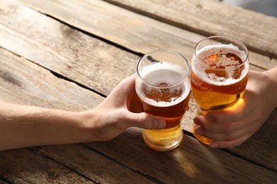 Photo of Friends with glasses of beer at wooden table, closeup