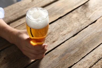Photo of Man with glass of beer at wooden table, closeup. Space for text