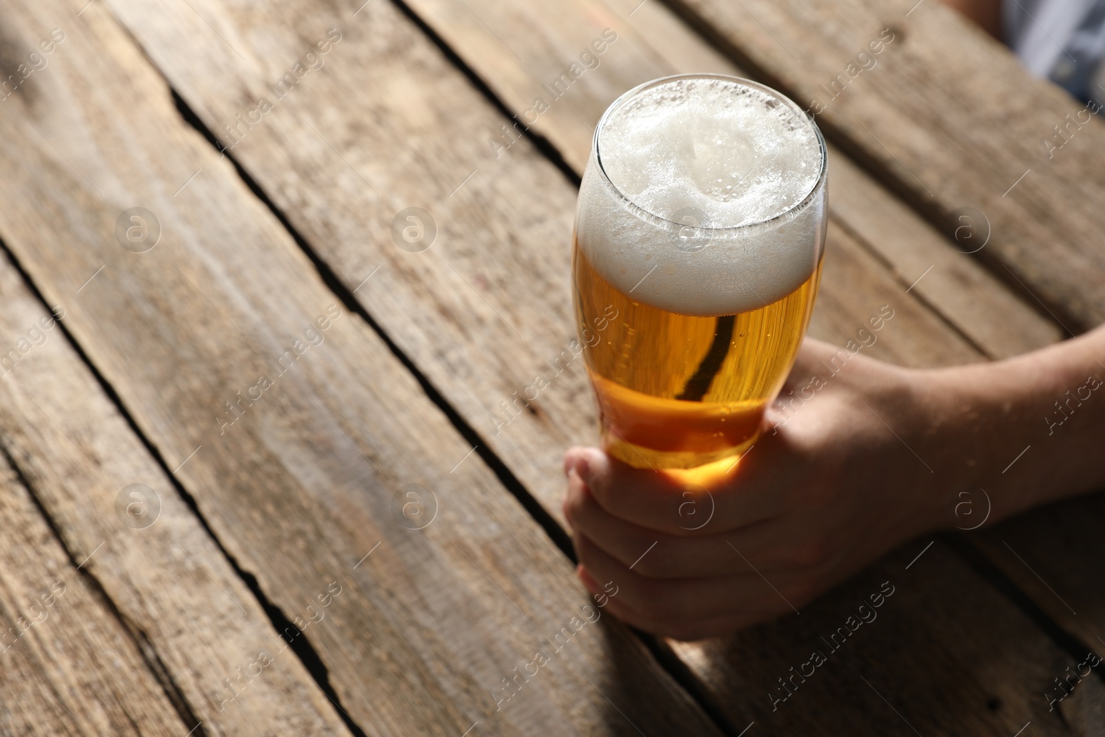 Photo of Man with glass of beer at wooden table, closeup. Space for text