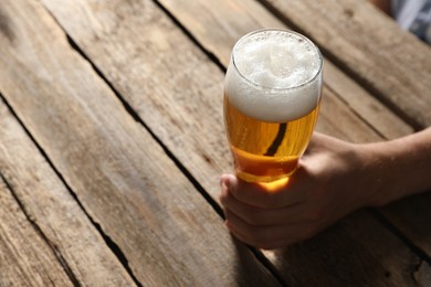Photo of Man with glass of beer at wooden table, closeup. Space for text