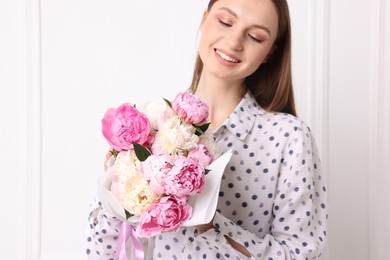 Photo of Woman with beautiful bouquet of peonies near white wall indoors