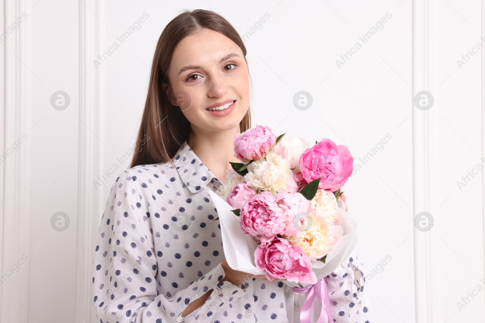 Photo of Woman with beautiful bouquet of peonies near white wall indoors