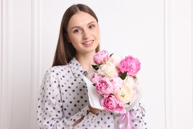 Photo of Woman with beautiful bouquet of peonies near white wall indoors