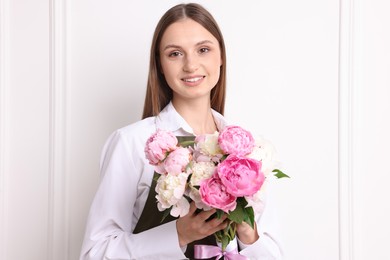 Photo of Florist with beautiful bouquet of peonies near white wall indoors
