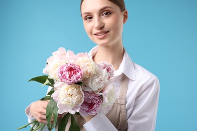 Photo of Florist with beautiful bouquet of peonies on light blue background