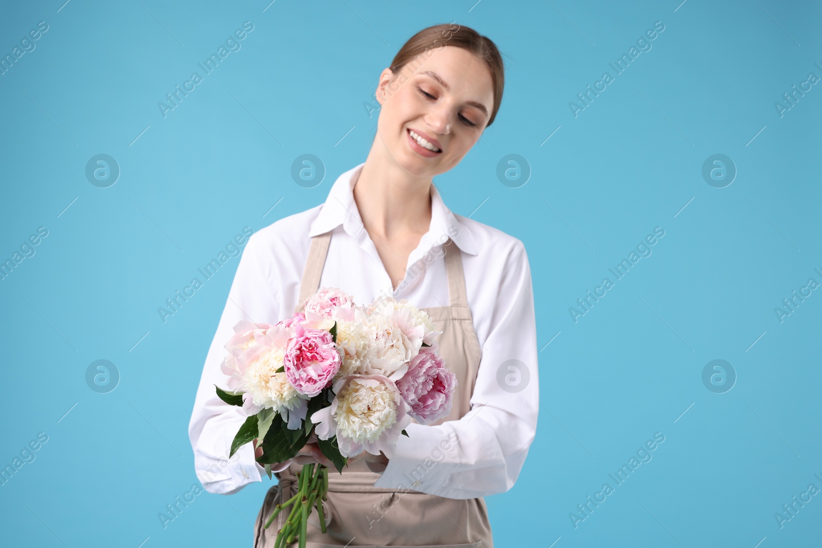 Photo of Florist with beautiful bouquet of peonies on light blue background