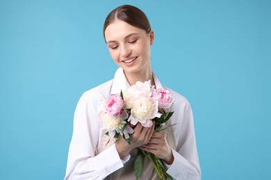 Photo of Florist with beautiful bouquet of peonies on light blue background