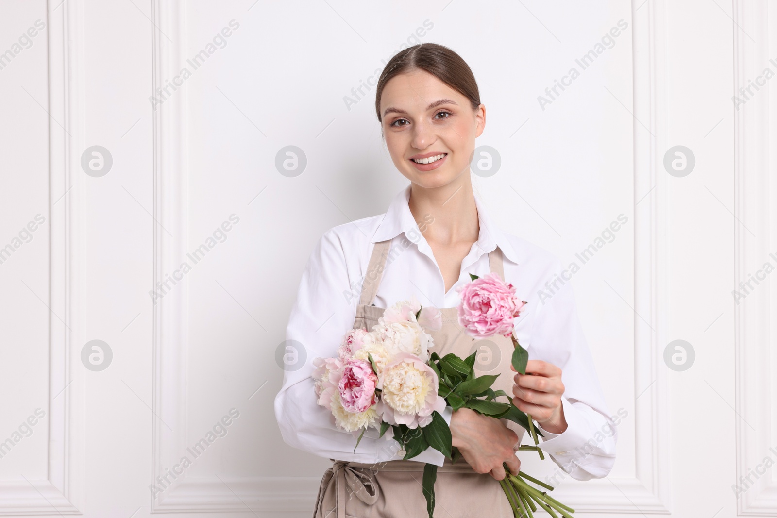Photo of Florist with beautiful bouquet of peonies near white wall indoors