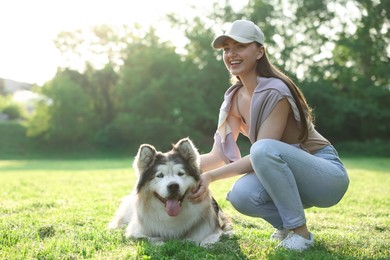 Photo of Smiling woman with her cute Alaskan malamute dog on green grass outdoors in morning